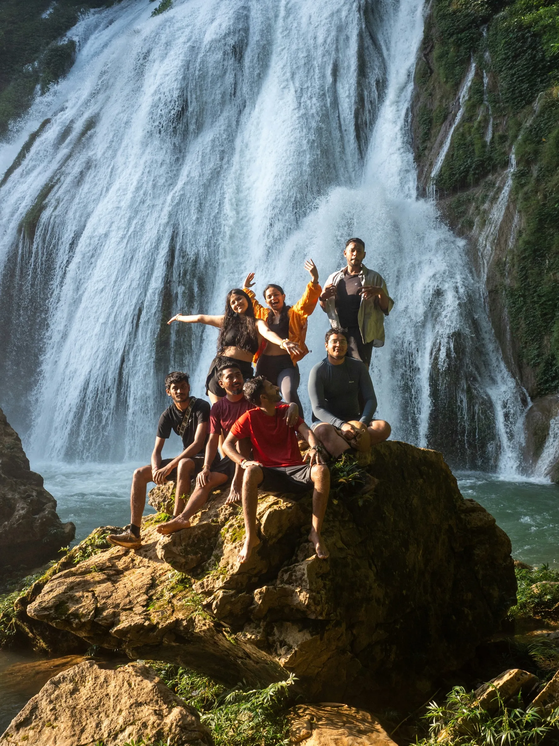 A tour group celebrating on the rocks beneath a waterfall